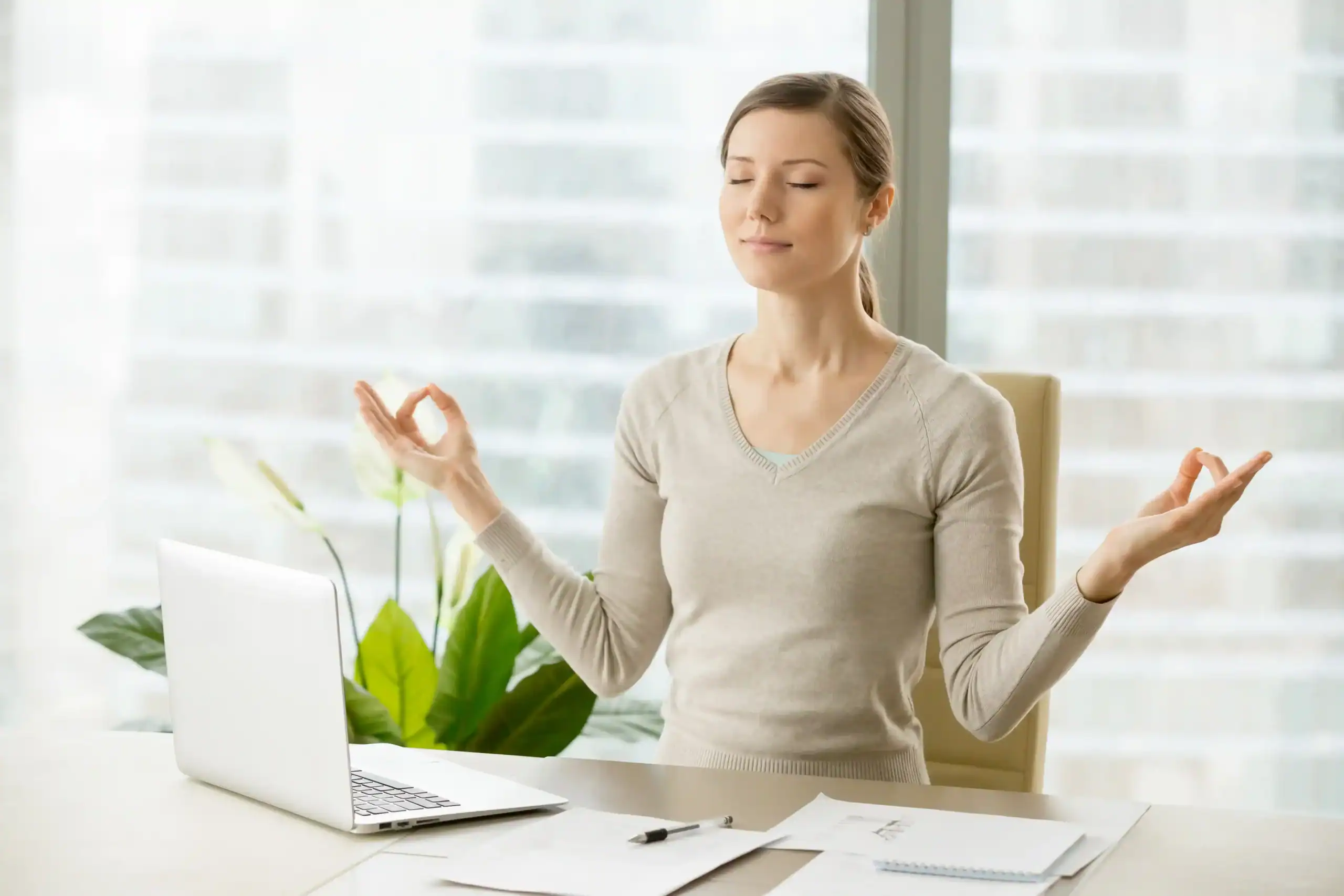 Person practicing deep breathing at an office desk, sitting upright with closed eyes, promoting relaxation and stress relief at work.