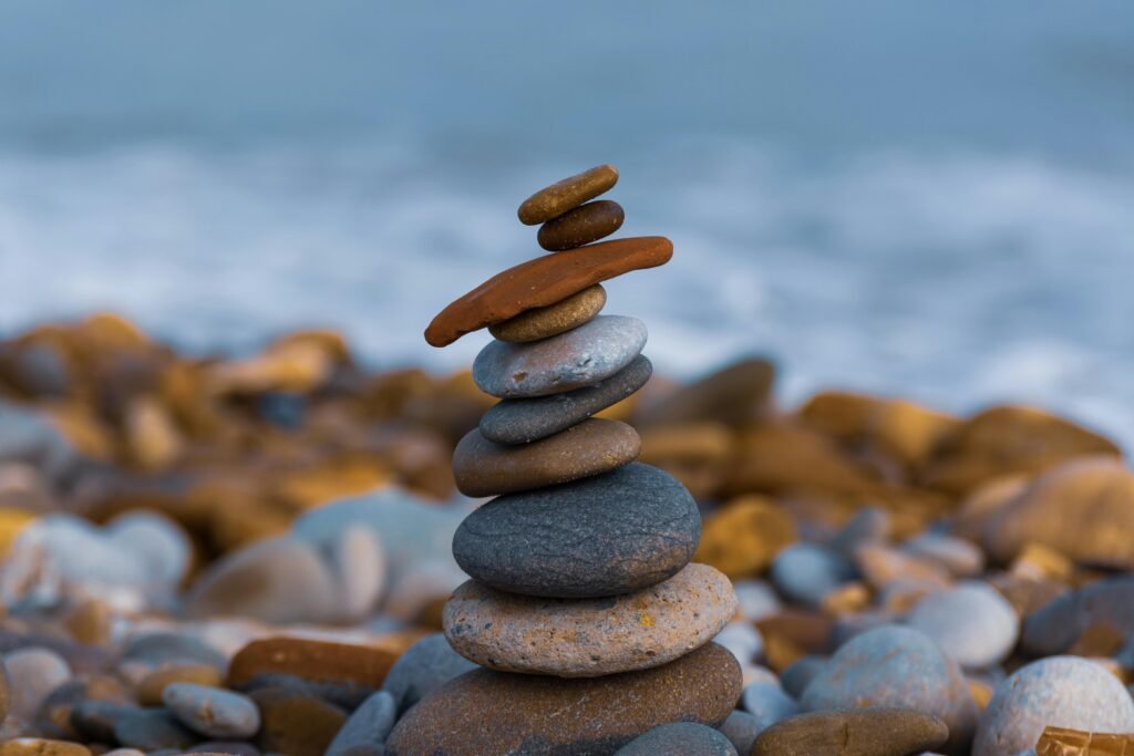 A realistic beach scenario with a small pile of balanced stones of indifferent sizes lying on a bed of pebbles; the background shows a calm ocean with only small waves to give a peaceful and serene atmosphere.